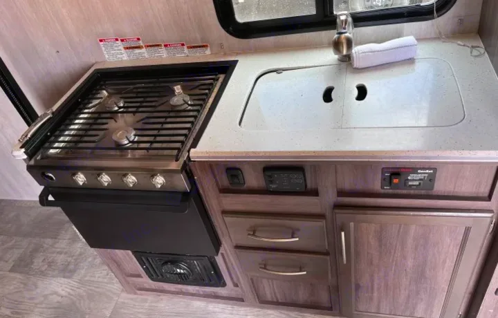 Compact kitchen in an RV rental, with a four-burner stove, covered sink, and control panel for comfortable trips.. Genesis Supreme Rv Genesis Supreme 2021