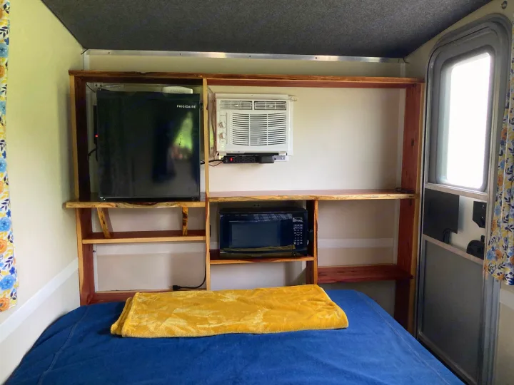 Cozy rv rental bedroom: bed, built-in shelves, mini-fridge, microwave, and AC unit provide a functional space.. Runaway Rouser 2023