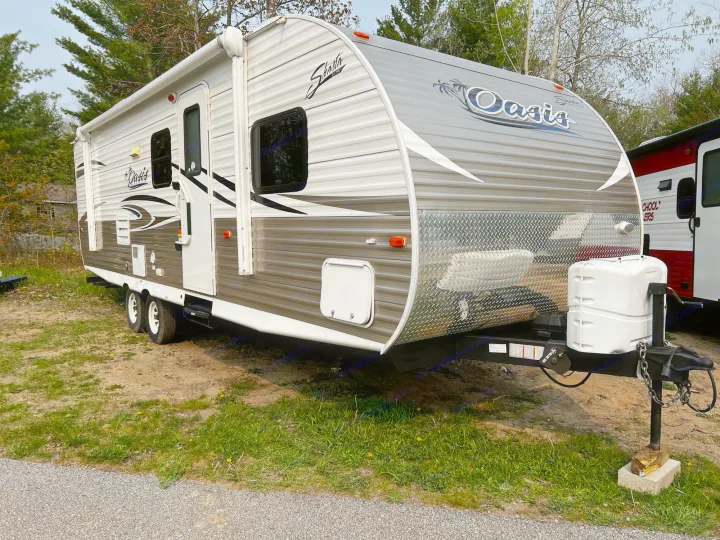 A Shasta Oasis travel trailer, ideal for an rv rental, parked on grass. Note the awning and front propane tank.. Shasta Oasis 2016
