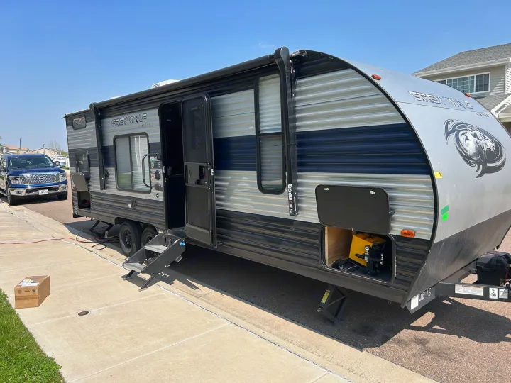 This large RV rental travel trailer is parked with its door open, steps down, and a blue truck nearby on a sunny day.. Forest River Cherokee Grey Wolf Special Edition 2022