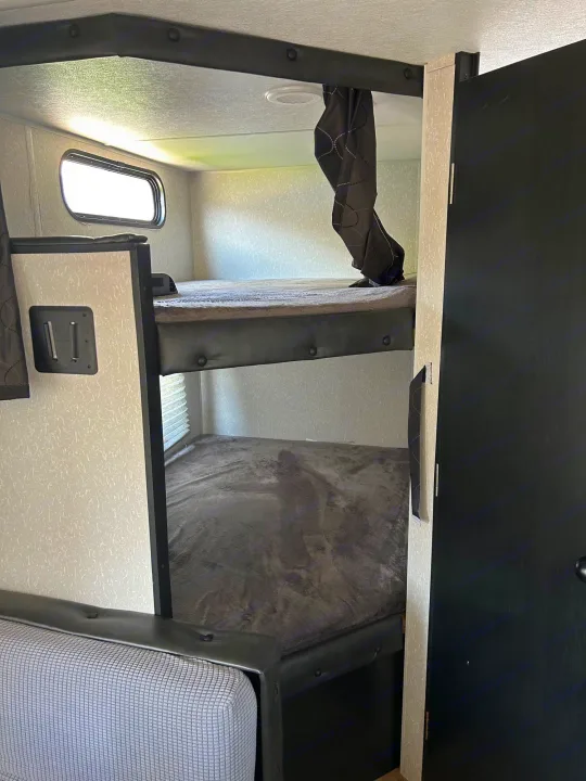 RV rental interior showing stacked bunk beds with grey blankets, a window, and a door. Cozy camper sleeping.. Forest River Cherokee Grey Wolf Special Edition 2022