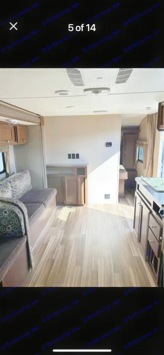Spacious RV rental interior featuring a living area, kitchen with wood cabinets & sink, a bed in the background, and wood-look flooring.. Shasta Oasis 2016