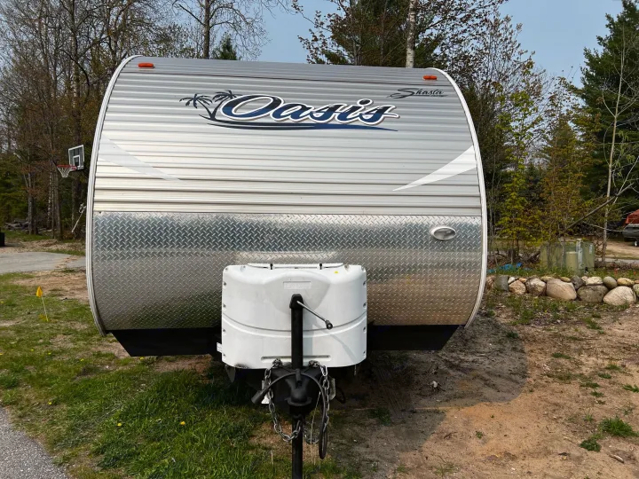 Front view of a silver Shasta Oasis travel trailer, with diamond plate lower half and white LP gas cover. Ideal for RV rental.. Shasta Oasis 2016