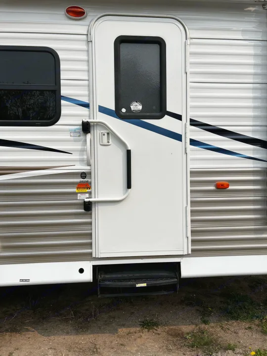 Side view of an rv rental's main entry, featuring a white door, grab handle, and fold-down steps. Striped exterior and window.. Shasta Oasis 2016