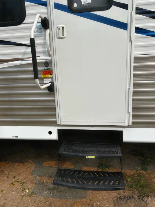 RV rental's entry: white camper door, black steps, and grab handle, parked on dirt.. Shasta Oasis 2016