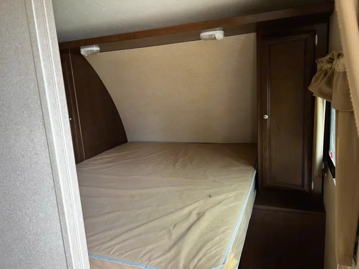 RV rental camper bedroom: Features a bed with light sheets, dark wood cabinets, and two overhead reading lights.. Shasta Oasis 2016