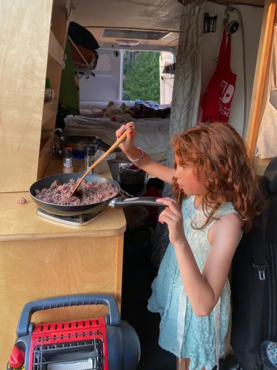 Cooking in our RV rental! A girl stirs ground meat on a portable stove inside the camper van kitchen.. Mercedes-Benz Sprinter 2017