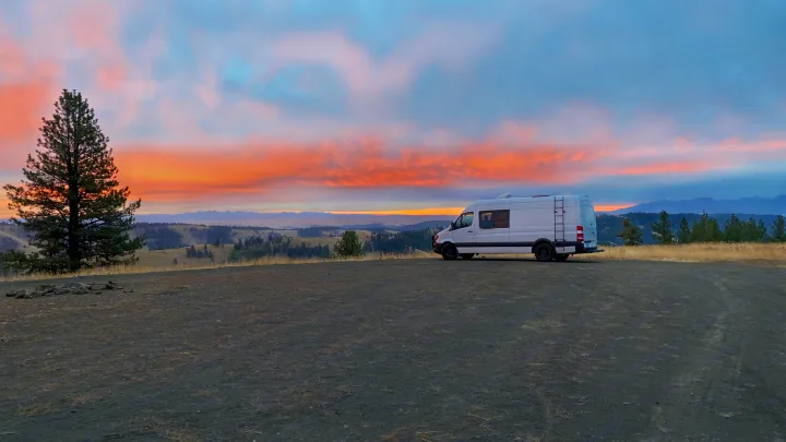 White **RV rental** camper van at a scenic overlook, capturing a vibrant sunset over distant mountains & forests.. Mercedes-Benz Sprinter 2017