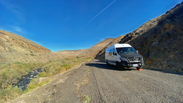 RV rental exploring a scenic gravel road alongside a creek in arid mountains. Perfect for van life adventures!. Mercedes-Benz Sprinter 2017