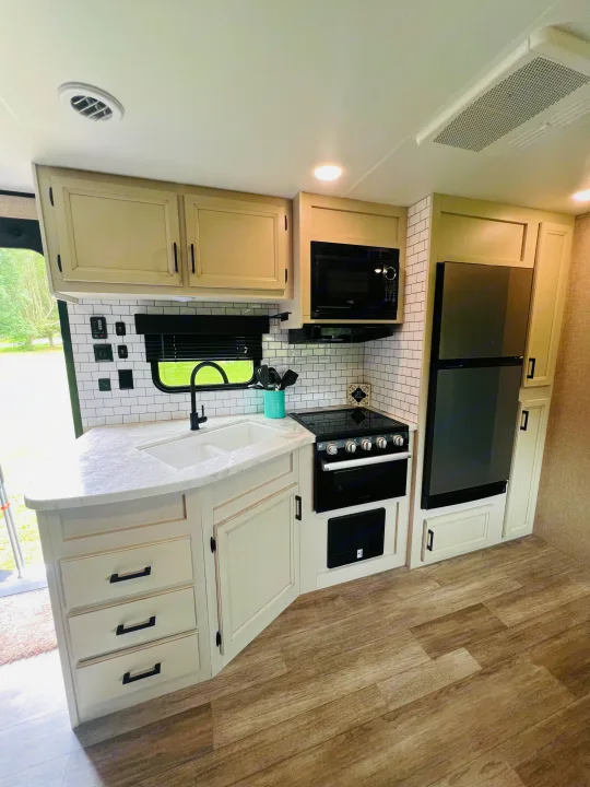 Enjoy modern comforts in this RV rental kitchen, complete with white cabinets, subway tile, sink, stove, microwave, and fridge.. Jayco Jayflight 324BDS 2023
