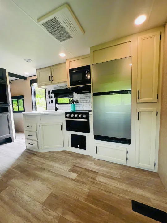 Modern RV rental kitchen with white cabinets, stainless steel appliances, subway tile, and wood-look flooring.. Jayco Jayflight 324BDS 2023