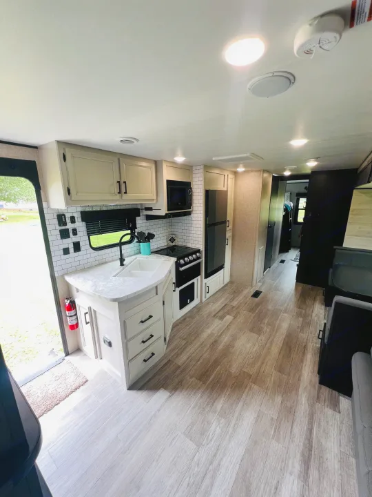 Modern RV rental interior featuring a well-equipped kitchen with white cabinets, a sink, stove, fridge, and stylish backsplash.. Jayco Jayflight 324BDS 2023