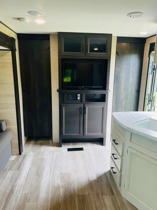 This modern rv rental features an entertainment center with TV, storage, light wood-look flooring, and a kitchen island.. Jayco Jayflight 324BDS 2023