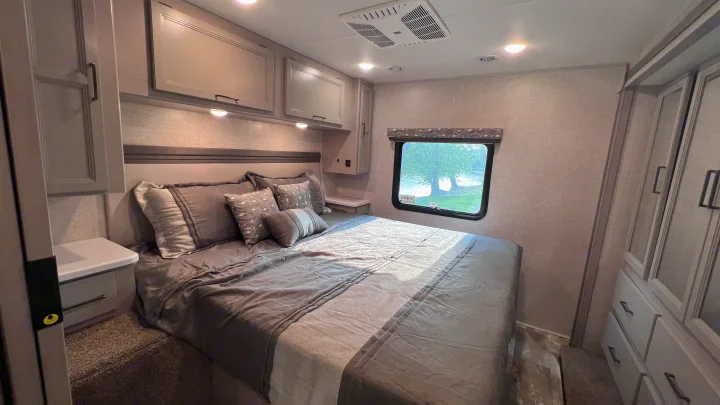Modern RV rental bedroom with a comfortable bed, gray bedding, ample built-in storage, and a window showcasing a scenic view.. Thor Windsport 2023