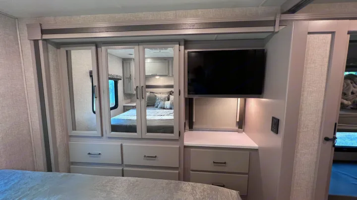 Modern RV rental bedroom featuring mirrored wardrobe, dresser, TV, and storage for comfortable travel.. Thor Windsport 2023