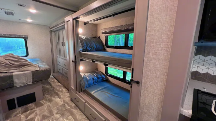 Cozy RV rental bedroom with a main bed, two bunk beds, and built-in storage. Ideal for family adventures.. Thor Windsport 2023