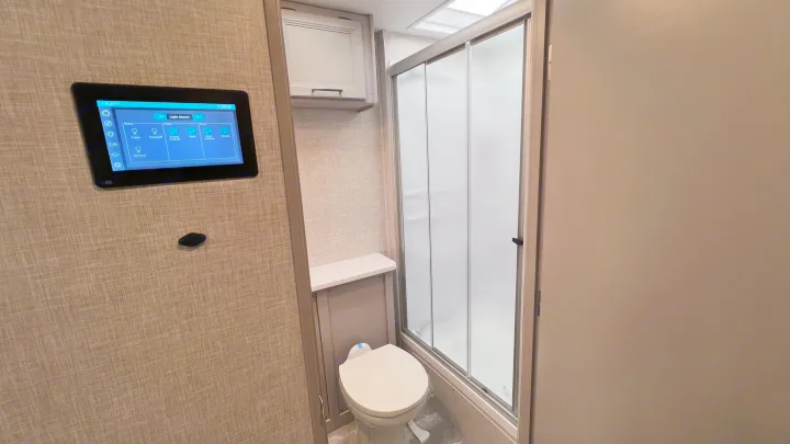 Compact RV rental bathroom: shower, toilet, and a digital light control panel on the wall.. Thor Windsport 2023