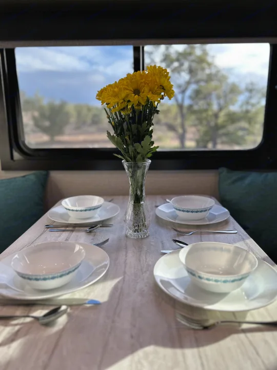 Cozy RV rental dining table set for four with bright yellow flowers, offering a beautiful view of nature outside.. Olympia Sport 2022