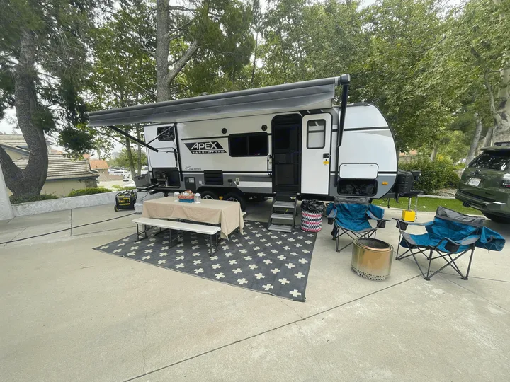 An RV rental provides a comfortable outdoor living space with an extended awning, table, benches, and fire pit.. Coachmen Apex Nano 2021