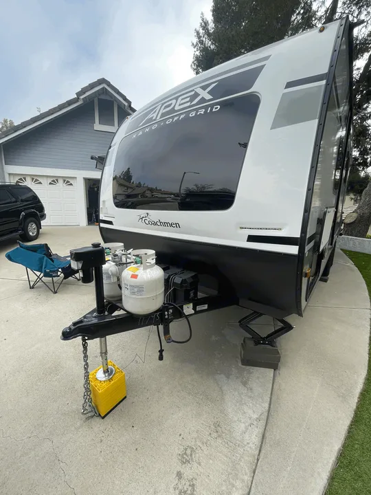 An Apex Nano Off Grid travel trailer, possibly an rv rental, is parked in a residential driveway with house and trees in background.. Coachmen Apex Nano 2021