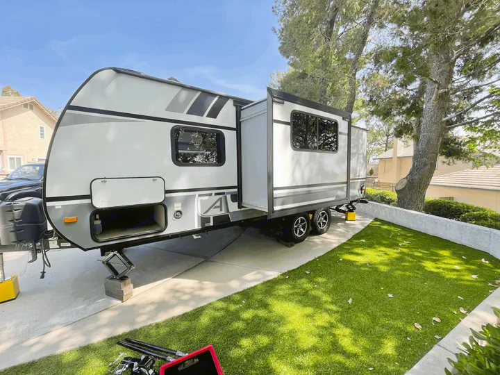 A modern grey RV rental (travel trailer) with its slide-out extended, parked on a driveway next to artificial grass.. Coachmen Apex Nano 2021