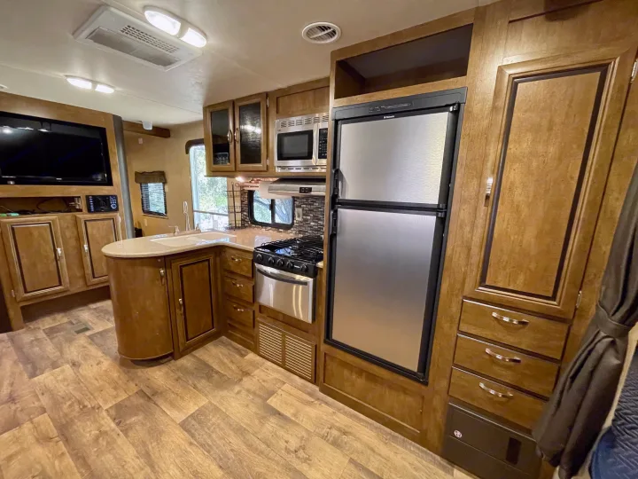 This RV rental kitchen features a stainless steel fridge, stove, microwave, and sink, with wood cabinetry and an entertainment center.. Forest River Wildwood 2016