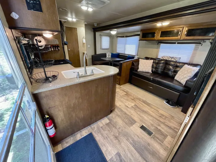 Bright rv rental interior showing kitchen, dinette, and dark leather sofa. Wood-look floors & fire extinguisher visible.. Forest River Wildwood 2016
