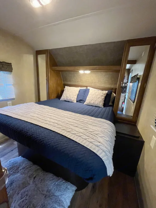 This cozy RV rental bedroom features a comfy navy blue bed with a knit blanket, built-in storage, and ambient lighting for travel.. Forest River Wildwood 2016