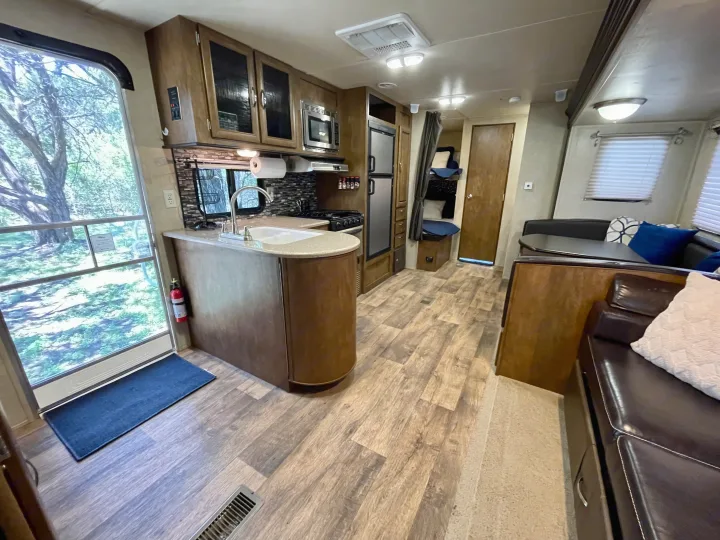 RV rental interior featuring a kitchen with a curved counter, dining area, and bunk beds. Wood-look flooring.. Forest River Wildwood 2016