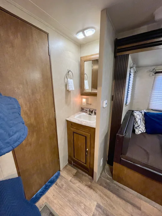 Compact RV rental interior featuring a functional bathroom vanity with sink and mirror, plus a cozy seating area.. Forest River Wildwood 2016