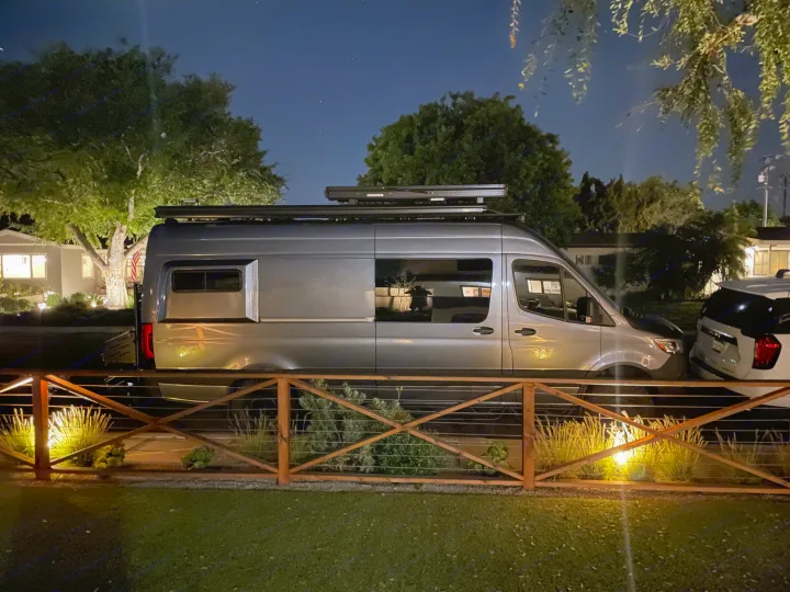 Experience freedom with this grey camper van, ideal for RV rental. Night scene shows the van parked on a street by a lit fence.. Mercedes-Benz Sprinter 2020