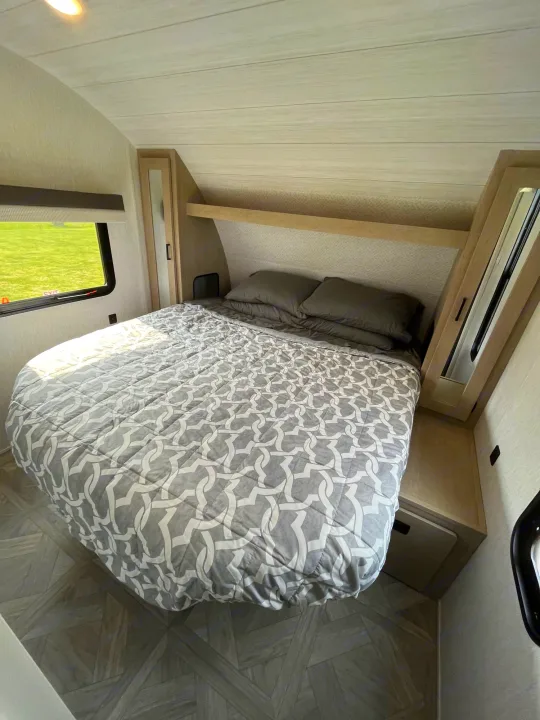 RV rental bedroom: a full bed with grey patterned comforter, window, and light wood interior.. Wildwood X-Lite BH 263 2023