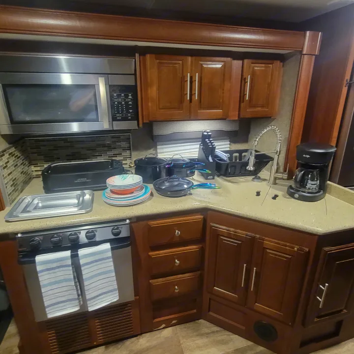 RV rental kitchen: stainless microwave, stove, sink, and cookware on stone-look counters. Ready for your mobile cooking.. Georgetown GT5 2017