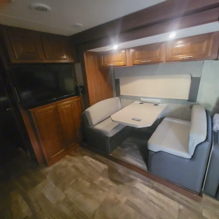 RV rental interior showcasing a dinette with benches and table, overhead cabinets, and a TV. Cozy living space for travel.. Georgetown GT5 2017
