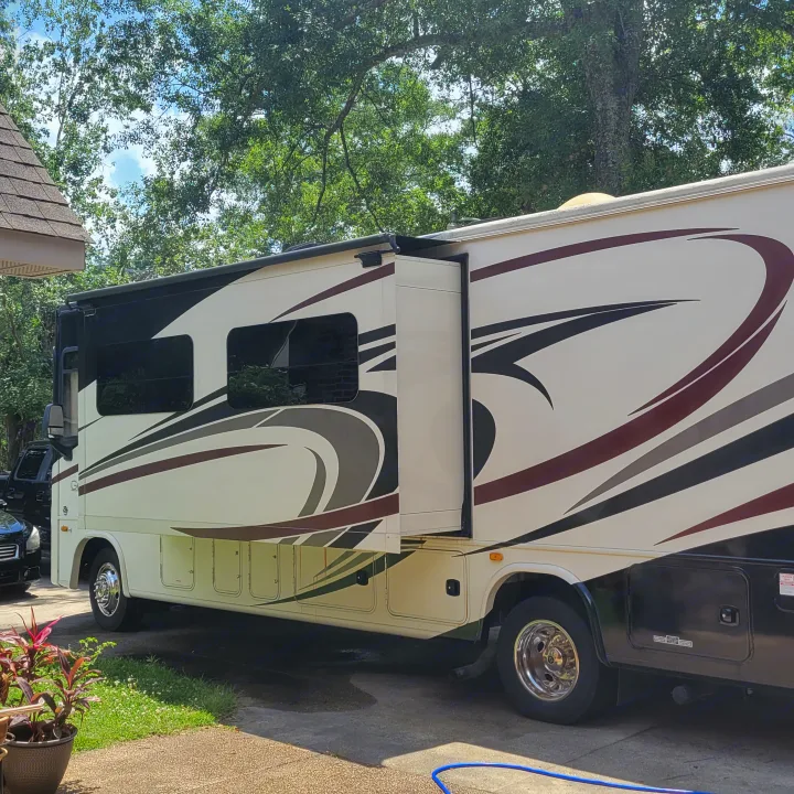 Large cream RV rental with extended slide-out parked on a sunny driveway amidst green trees.. Georgetown GT5 2017