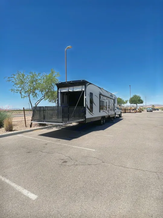 Spacious white toy hauler RV rental with its rear patio deployed, parked in an open lot under clear blue skies.. Genesis Supreme Rv Genesis Supreme 2020
