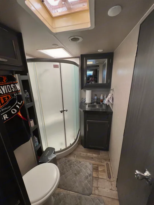 This image shows a compact RV rental bathroom with a curved shower, toilet, and sink vanity.. Genesis Supreme Rv Genesis Supreme 2020