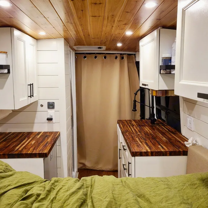 Bright RV rental interior with wood ceiling, white cabinetry, and warm wood counters. Features an integrated shower and inviting green bed.. Dodge RAM 3500 Promaster 159" Extended 2019