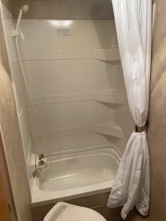 Compact RV rental bathroom interior featuring a clean shower/tub combo, handheld shower, and tied-back white curtain.. Keystone Hideout 2009