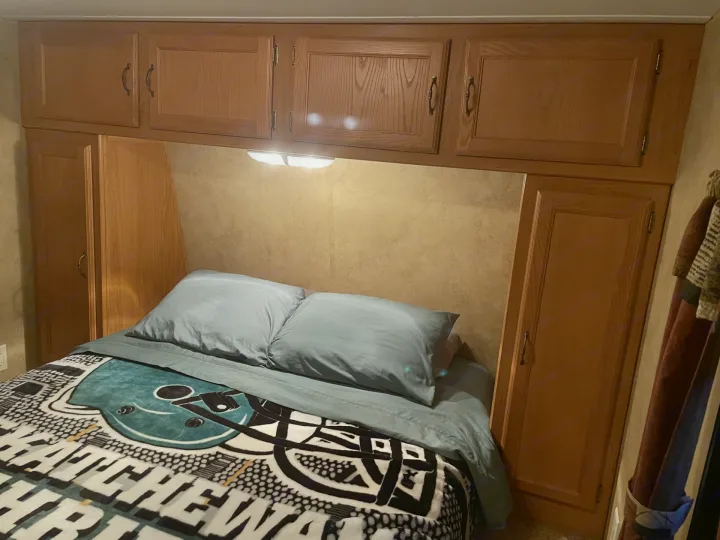 An RV rental bedroom with a bed, light blue bedding, overhead cabinets, side wardrobes, and a bright reading light.. Keystone Hideout 2009