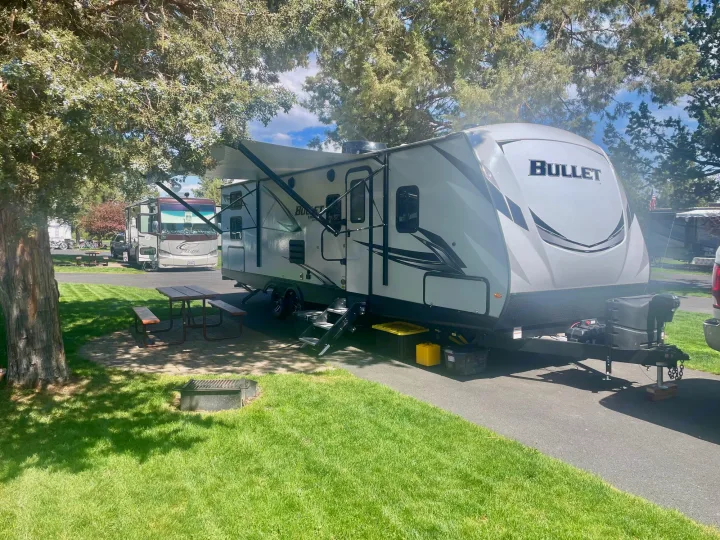 Our Bullet RV rental, with awning extended, offers a perfect retreat at this grassy RV park campsite with a picnic table.. Keystone Bullet 2021
