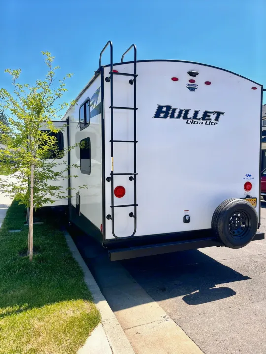 White Bullet Ultra Lite travel trailer, an RV rental, seen from the rear with ladder & spare tire mounted.. Keystone Bullet 2021