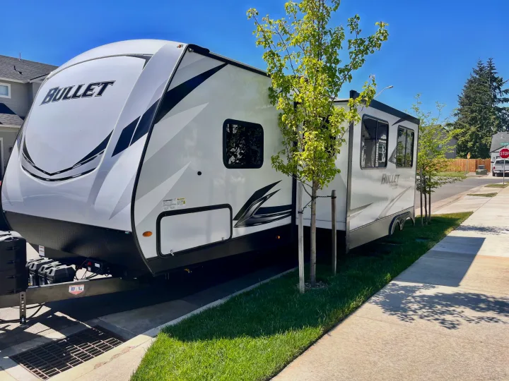 A white "BULLET" travel trailer, a great RV rental option, is neatly parked on a sunny residential driveway.. Keystone Bullet 2021