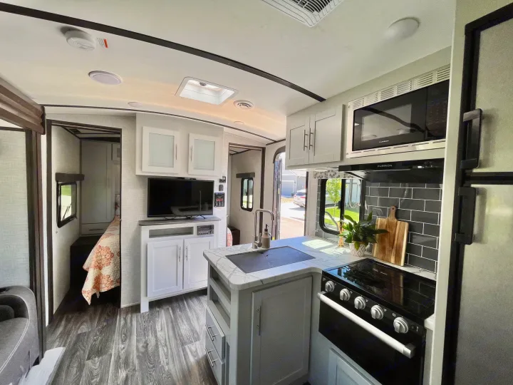 Stylish RV rental interior with a gray wood floor, modern kitchen, living area with TV, and bedroom. Your adventure awaits!. Keystone Bullet 2021