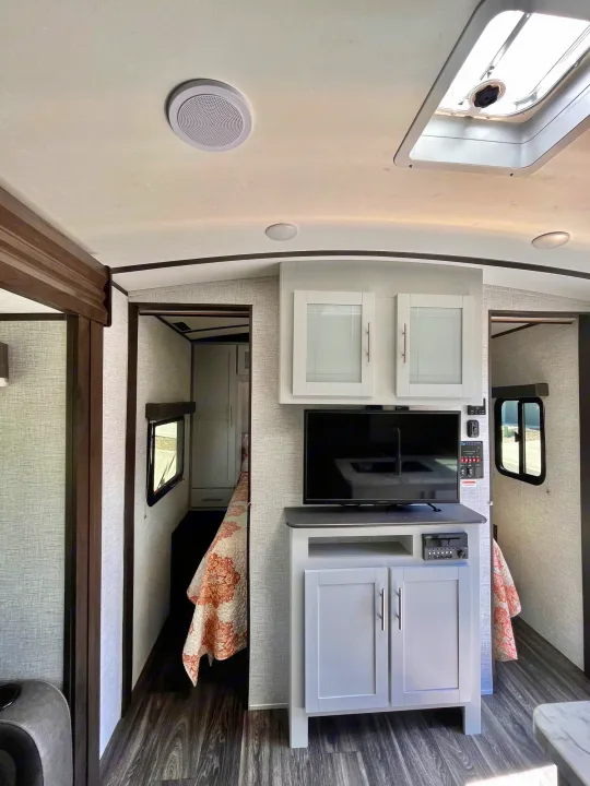 Spacious RV rental interior featuring a living area with TV, overhead cabinets, and a hallway leading to a bright bedroom.. Keystone Bullet 2021