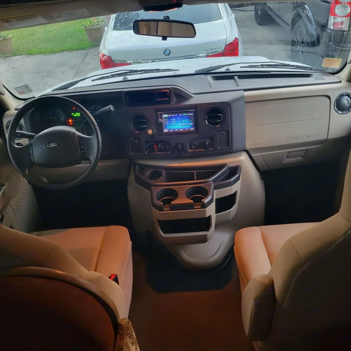 Driver's view of a Ford E-Series RV rental cockpit, showing the dashboard, steering wheel, radio, and front seats.. Forest River Coachmen Freelander 2016