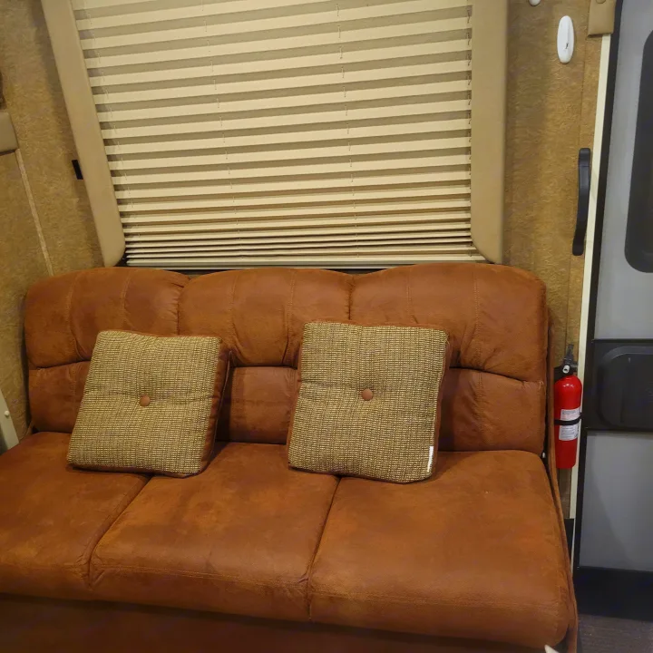 RV rental interior: cozy brown sofa with decorative cushions, pleated window blinds, & fire extinguisher for safety.. Forest River Coachmen Freelander 2016