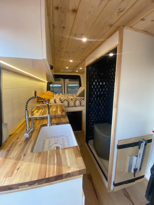 Explore this stylish rv rental camper van's interior: a wooden kitchen, cozy bed, and compact tiled bathroom.. Mercedes-Benz Sprinter 2022