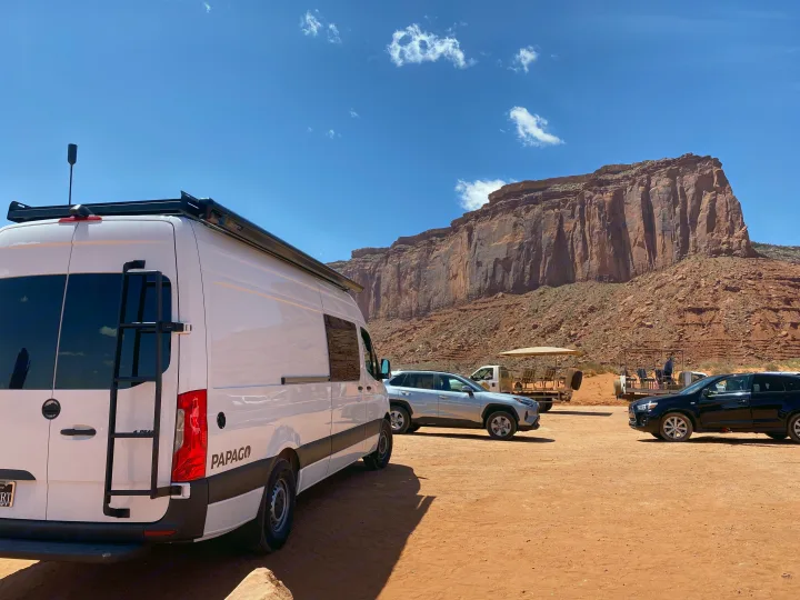 White RV rental parked on red dirt. Majestic red rock cliffs rise under a clear sky.. Mercedes-Benz Sprinter 2022