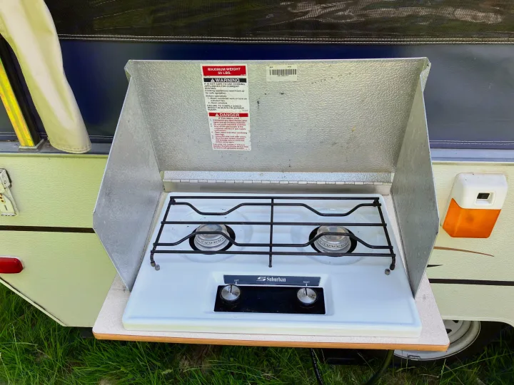 An outdoor two-burner stove, part of an RV rental, extends from a camper, ready for cooking with its wind guard up.. Jayco Qwest 2003